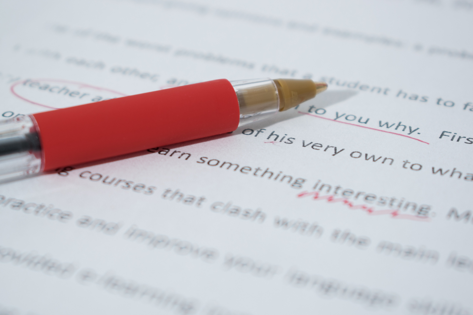 Ein Stift liegt auf einem Papier. Im Text sind Stellen mit rot markiert.