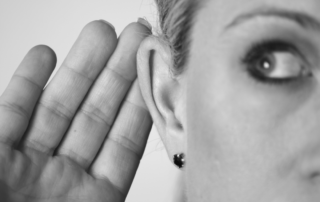 Eine Frau hält sich ihre Hand ans Ohr um besser zu verstehen