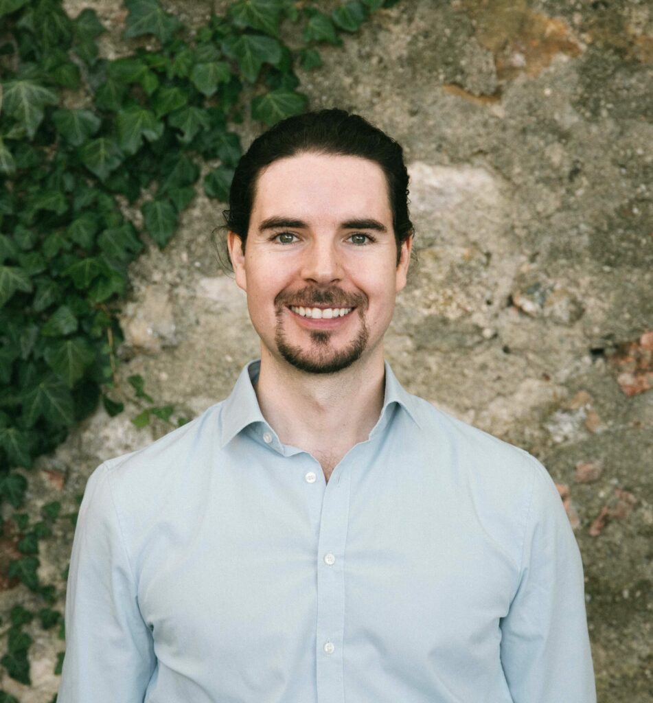 Tobias Urban steht lächelnd vor einer Mauer